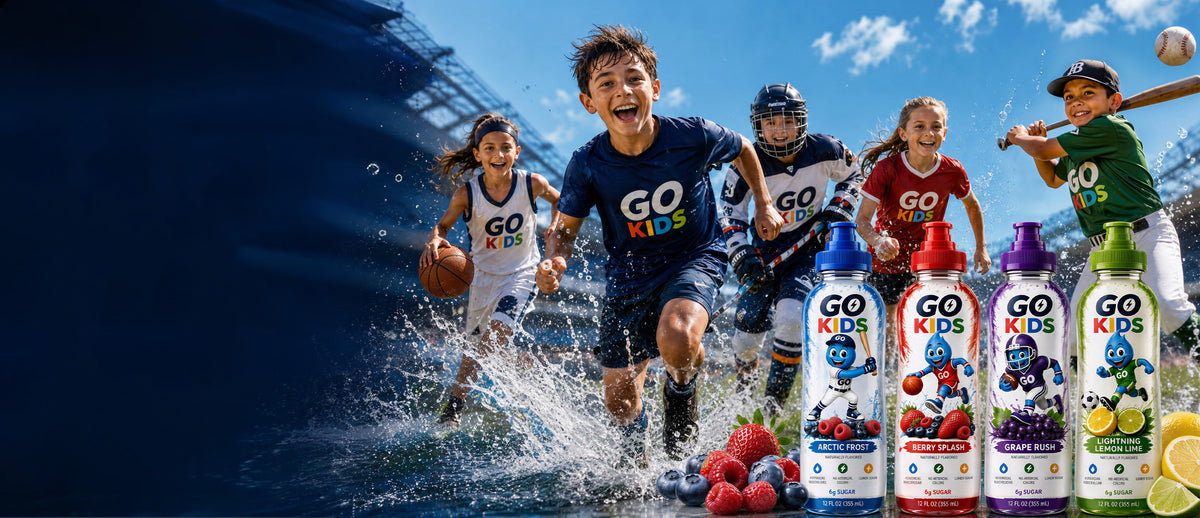 A group of children playing sports in a stadium scene with water splashes, alongside several bottles of Go Kids drinks in front of them. The bottles show colorful labels with cartoon characters and fruit imagery, including red, blue, green, and purple flavors.